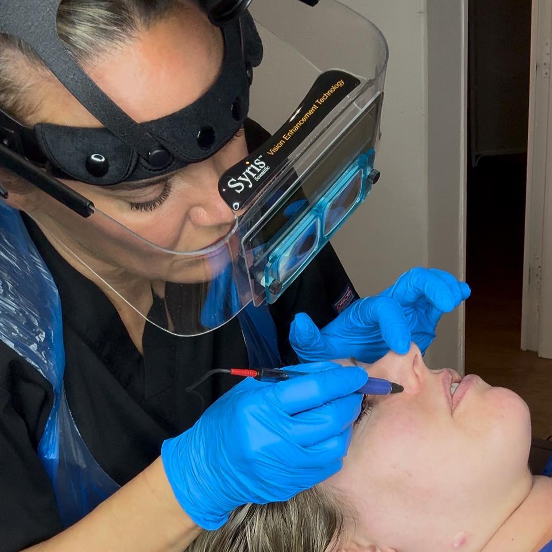 Beauty therapist carrying out a professional eyebrow treatment using precision equipment in a safe and hygienic salon environment.